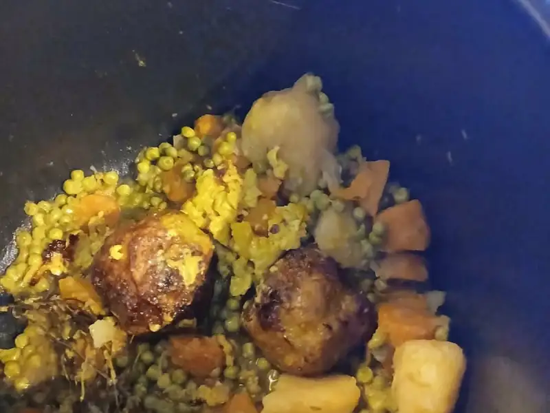 Bolinhos de ervilha, cenoura e batata com curry, cozidos em uma panela de barro preta.