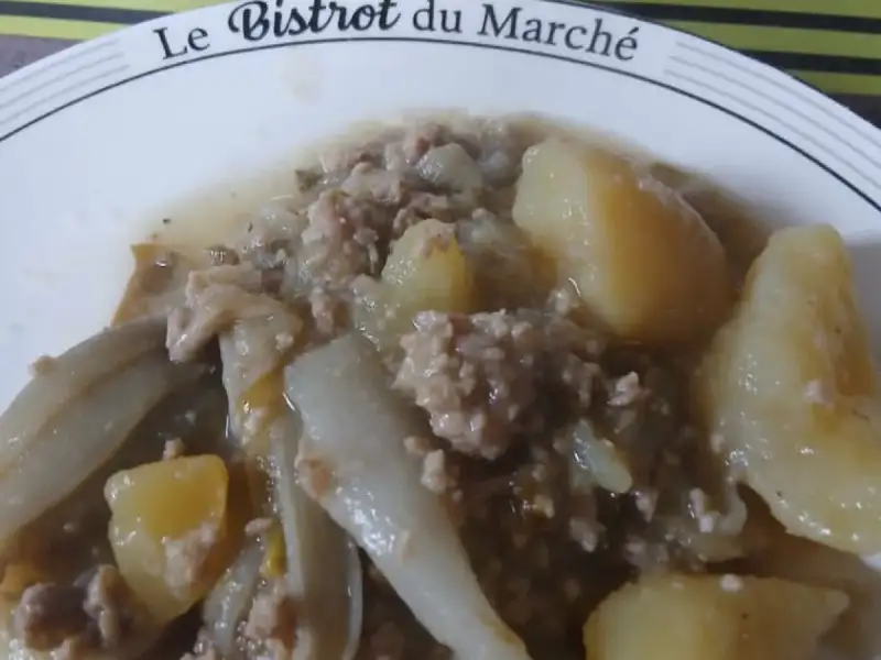Prato com endervias refogadas, carne moída e batatas, com uma panela de aço inoxidável ao fundo.