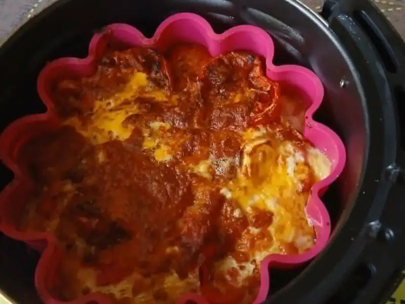Clafoutis de tomate com queijo gratinado, assado em uma forma de silicone rosa, dentro de uma air fryer.