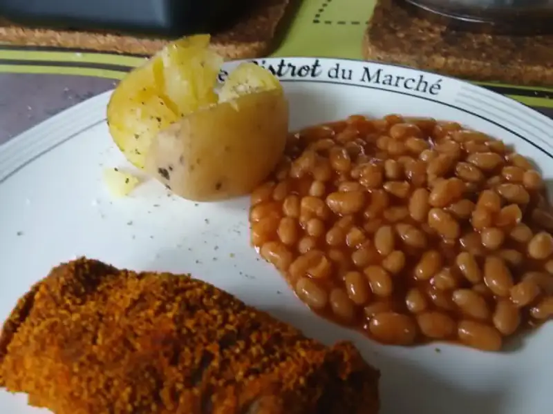 Frango empanado crocante com páprica, feijão branco com molho de tomate e batata palha servidos em uma travessa.