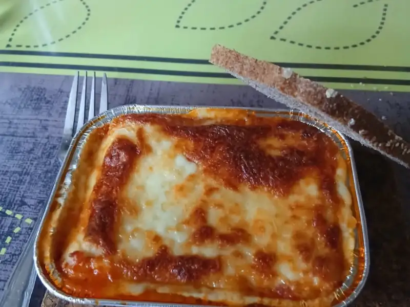 lasanha individual, feita em casa: um recipiente de alumínio bem gratinado, com uma fatia de pão tostado.