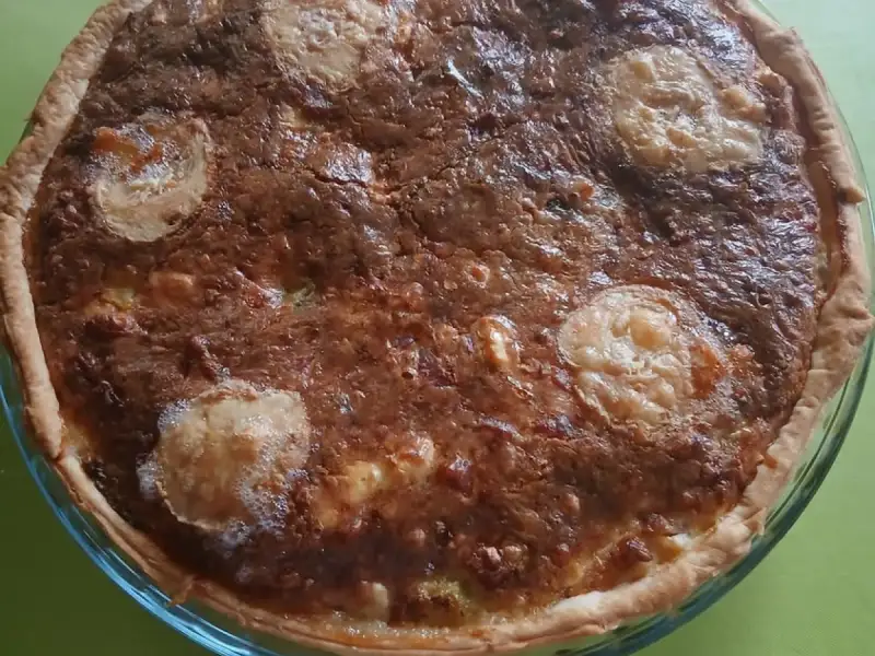 Quiche feita com sobras do refrigeração, bem dourada, com fatias de queijo de cabra, em uma forma de vidro.