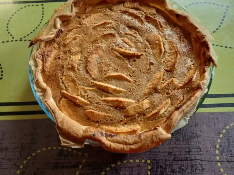 Torta de maçã alsaciana dourada, com fatias de maçã incorporadas na massa, em um recipiente de vidro.