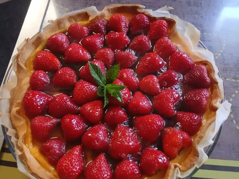 Torta de morangos caseira, com morangos inteiros sobre creme de confeiteiro, decorada com hortelã, em um recipiente de vidro.